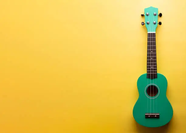 Green ukulele on a yellow background.