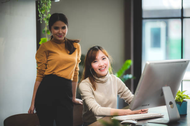 istock Group of international university students having fun studying in library, two colleagues of modern co-working space talking and smiling while sitting at the desk table with computer 1214481430