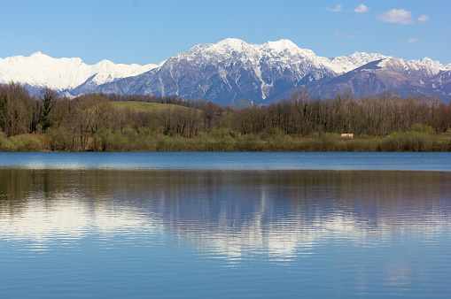 Small lake of Ragogna, near San Daniele del Friuli, Italy, in late winter, with the snow-capped mountains in the background