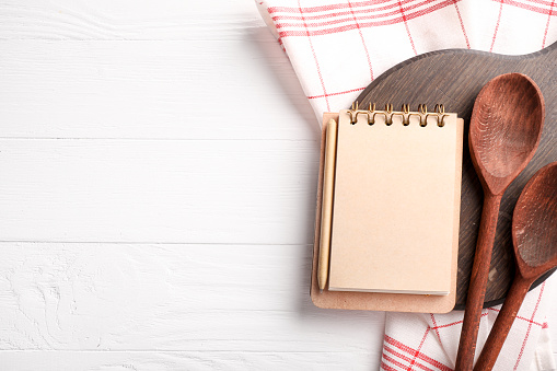 Recipe book, wooden spoons and board on white wooden background