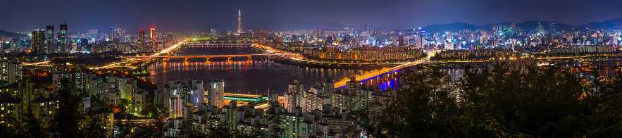 Highrise cityscape and glittering neon night skyscrapers along the tranquil waters of the Han River in the heart of Seoul, South Korea’s vibrant capital city.