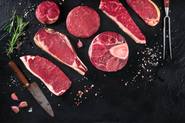 diverses coupes de viande, tirées du haut sur un fond noir avec du sel, du poivre, du romarin et des couteaux, avec l’espace de copie - red meat steak meat food photos et images de collection