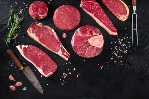 vari tagli di carne, girati dall'alto su sfondo nero con sale, pepe, rosmarino e coltelli, con spazio per la copia - meat steak veal beef foto e immagini stock