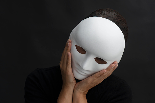 Sad person is holding white mask in front of its face.