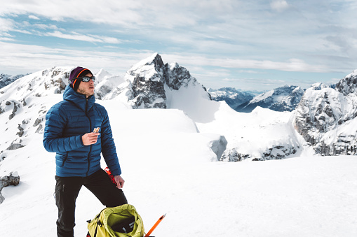 Extreme sport concept stock photo, young male Caucasian practicing winter mountaineering. Way to the top is strenuous but the view makes you forget about everything. Having a snack at the top, enjoying the view.