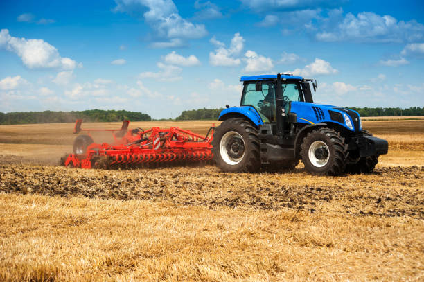 istock blue new tractor pulls a red harrow raises dust at the field, soil preparation 1214493185