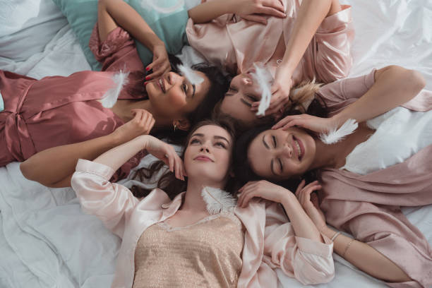 istock Selective focus of multicultural women resting together on bed with feathers at bachelorette party 1214494038