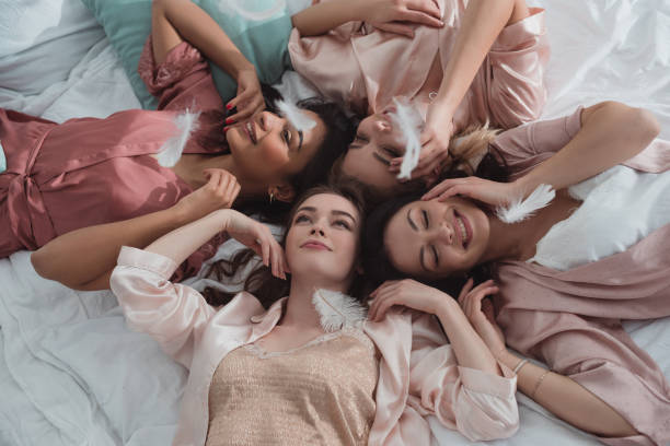 Selective focus of multicultural women resting together on bed with feathers at bachelorette party Selective focus of multicultural women resting together on bed with feathers at bachelorette party bachelorette party stock pictures, royalty-free photos & images
