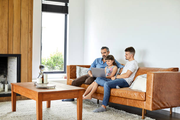 istock Gay men sitting with girl using laptop on sofa 1214494364
