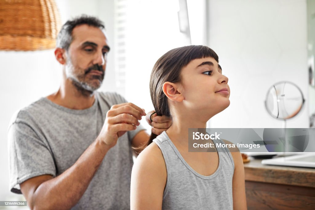 Gay man is tying daughter's hair in bathroom Cute girl with mature homosexual father in bathroom. Gay man is tying daughter's hair. They are in nightwear at home. Father Stock Photo