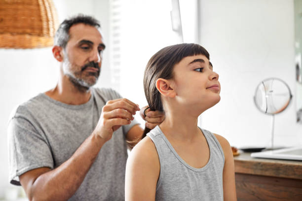 Gay man is tying daughter's hair in bathroom Cute girl with mature homosexual father in bathroom. Gay man is tying daughter's hair. They are in nightwear at home. leanincollection stock pictures, royalty-free photos & images