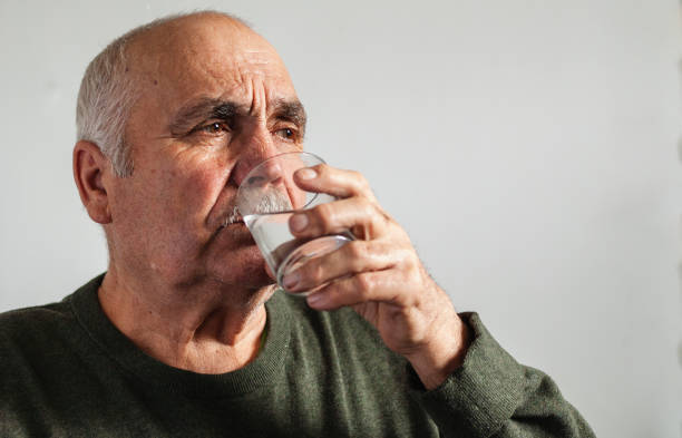 istock Elderly man taking medication with water 1214495577