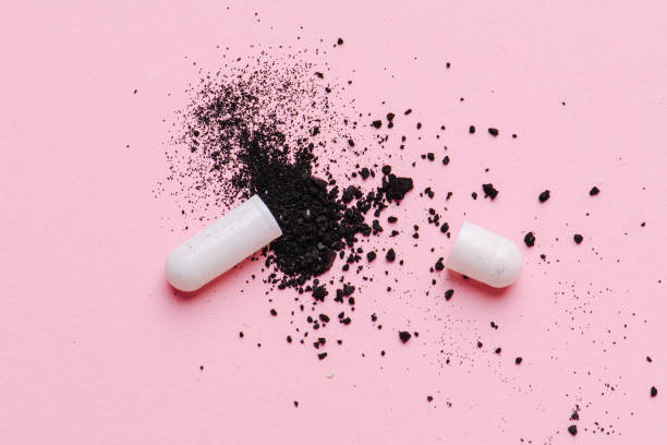 Open drug capsule causes black ingredient to splash over nearby surface stock photo