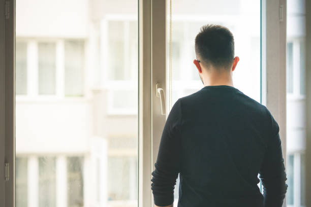 istock Man looking through the apartment window 1214496762