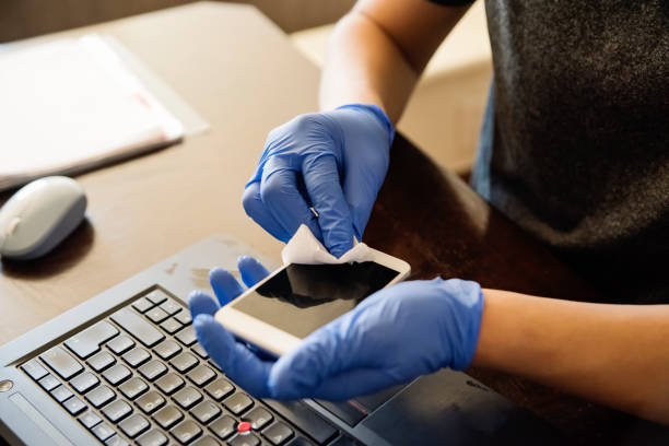 istock Man hands with gloves wiping mobile phone while working from home. 1214497323