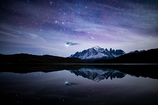 Torres del Paine Mountains in Patagonia reflected on the surface of a lake during the night with stars and the milky way, postcard of the National Park