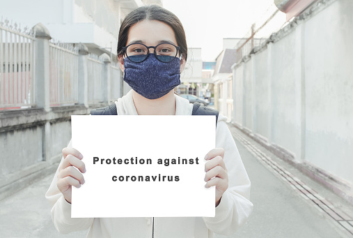 Asian women wearing mask  protective gear to protect coronavirus in China. holds the text is protection against sign paper as Campaign to reduce the risk of spreading the virus, coronavirus concept
