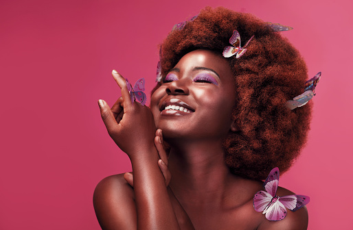 Studio shot of a beautiful young woman smiling while posing with butterflies in her hair against a purple background