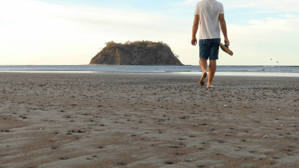 l’homme marche le long de la plage au lever du soleil - shorts rear view summer beach photos et images de collection