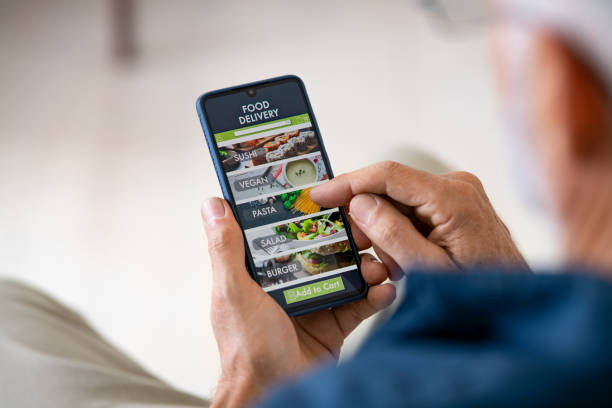 Man using mobile app to order delivery food Top view of man hands holding smartphone while order food delivery at home. Back view of mature man using food delivery app with mobile phone to order lunch. ordering stock pictures, royalty-free photos & images