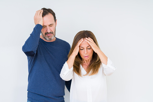 Beautiful middle age couple in love over isolated background suffering from headache desperate and stressed because pain and migraine. Hands on head.