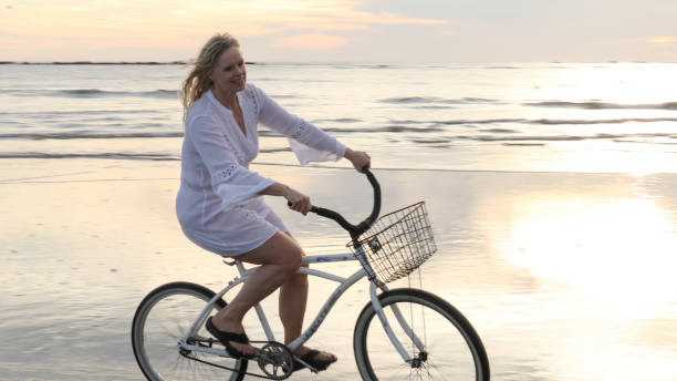 istock Woman rides bicycle down tropical beach at sunrise 1214514639
