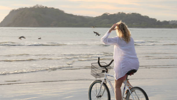 istock Woman rides bicycle down tropical beach at sunrise 1214514702