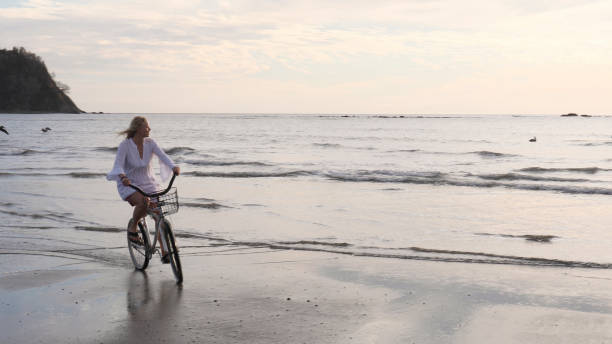 istock Woman rides bicycle down tropical beach at sunrise 1214514722