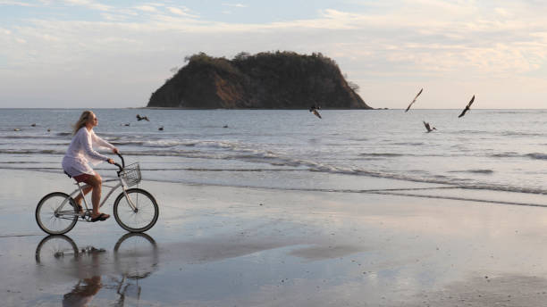 Woman rides bicycle down tropical beach at sunrise