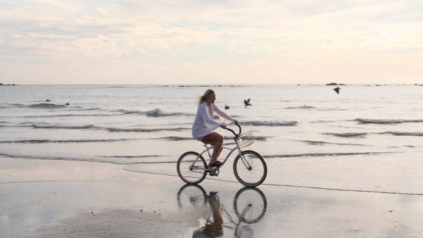 istock Woman rides bicycle down tropical beach at sunrise 1214514758