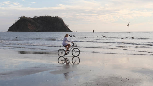 istock Woman rides bicycle down tropical beach at sunrise 1214514759