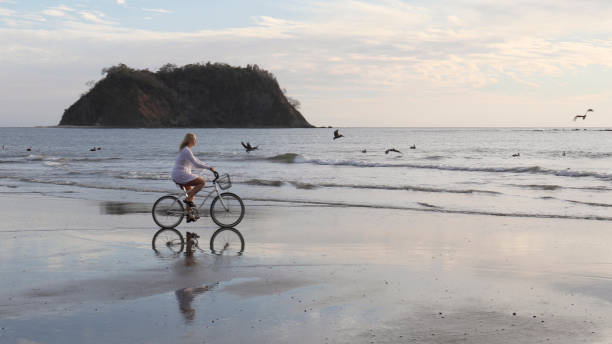 istock Woman rides bicycle down tropical beach at sunrise 1214514773