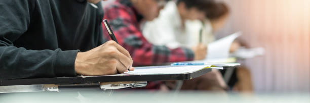Exam at school with student's taking educational admission test in class, thinking hard, writing answer in university classroom, education and world literacy day concept