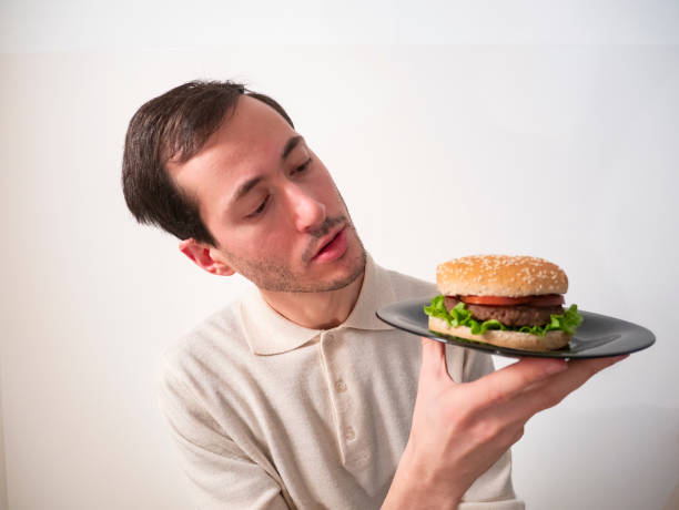 istock Handsome young man holding, looking and examining tasty hamburger for hexamination 1214518493