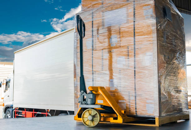 istock White truck cargo docking load shipment goods pallet, Hand pallet truck with heavy stack package boxes on pallet, Freight industry delivery logistics and transport. 1214520103