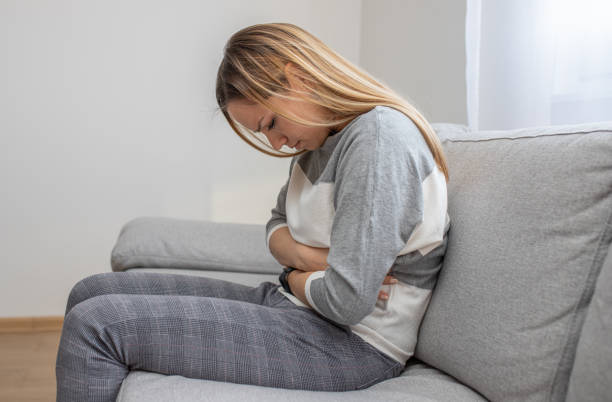 istock Girl with stomach ache sitting on sofa 1214520231