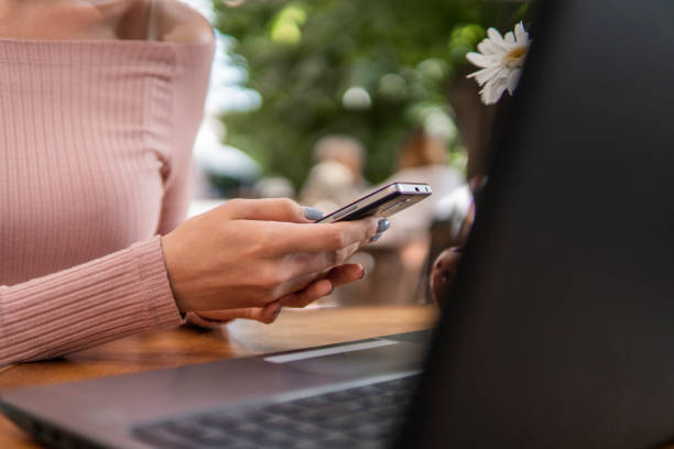 istock Modern business woman is reading incoming sms message on smartphone or watching broadcasting online on modern mobile phone while sitting in caffe with a laptop. Female student sitting in coffee. 1214522026