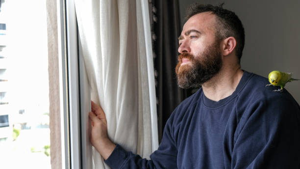 istock Man Looking Outside with Budgerigar on His Shoulder 1214522349