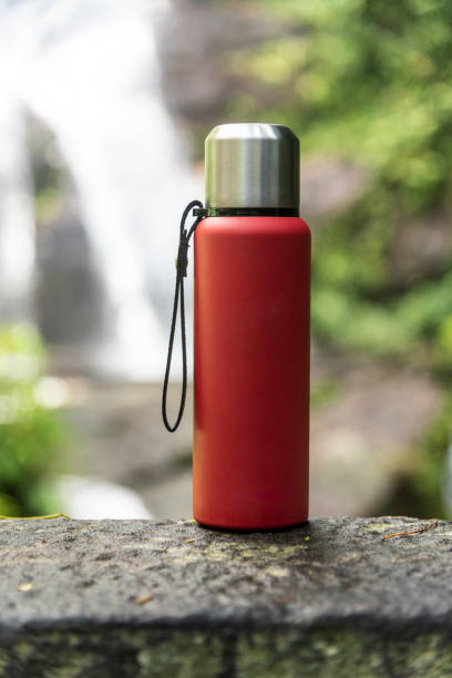 istock Red thermal bottle over rocky surface with waterfall on the back 1214522580