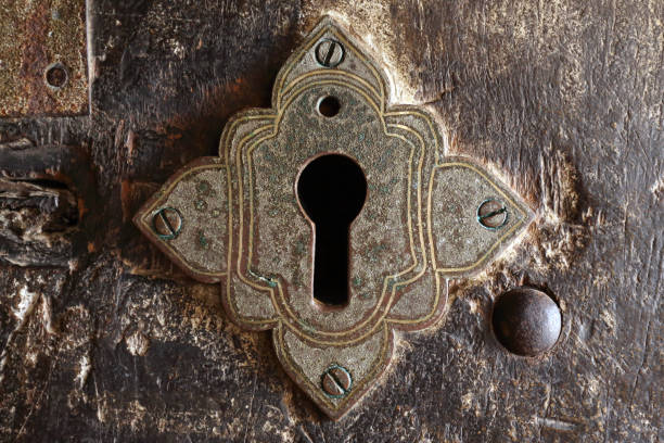 Ancient keyhole An ancient keyhole on a door to a Buddhist cave temple. The old metal keyhole is engraved and ornate, held by screws in the thick wooden door, which has large round headed metal nails close to the edge of the door frame. The door is worn down and weathered from many hundreds of years of use. It is covered in scratches and marks from the hands that have opened and closed it over the years. antique key stock pictures, royalty-free photos & images