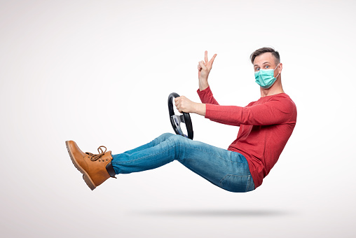 Man in a respiratory mask with a car steering wheel gives a victory sign with his hand. Attention virus concept