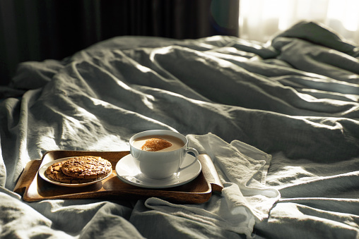 Breakfast - coffee with chocolate chip cookies on a wooden tray in a blue bed. Sunny cozy morning, leisurely and calm. Modern stylish food lifestyle. A lot of space for text.