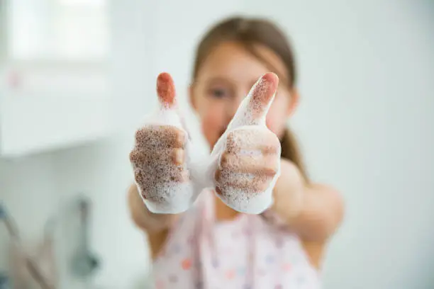 Photo of Little girl washing hands with water and soap in bathroom.