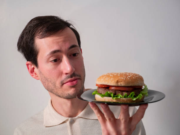 istock Handsome young man with interested facial expression, holding tasty hamburger 1214532440