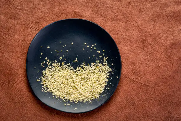 Hemp seed hearts on a black plate against brown, textured paper with a copy space, superfood concept