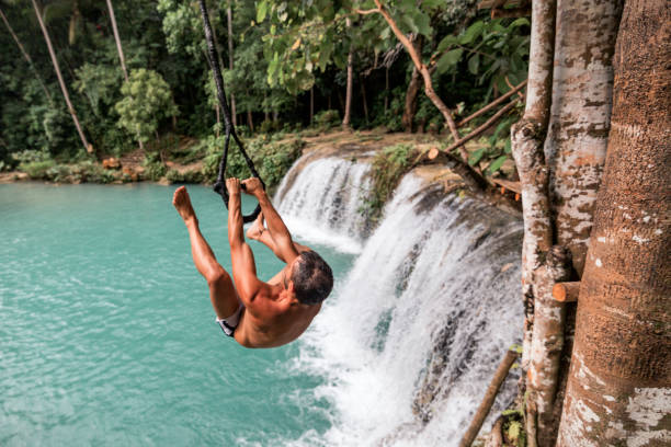 A young caucasian man plays with a rope swing over the Cambugahay Falls in Siquijor Island, Philippines A man playing with a rope swing in Cambugahay Falls siquijor island stock pictures, royalty-free photos & images