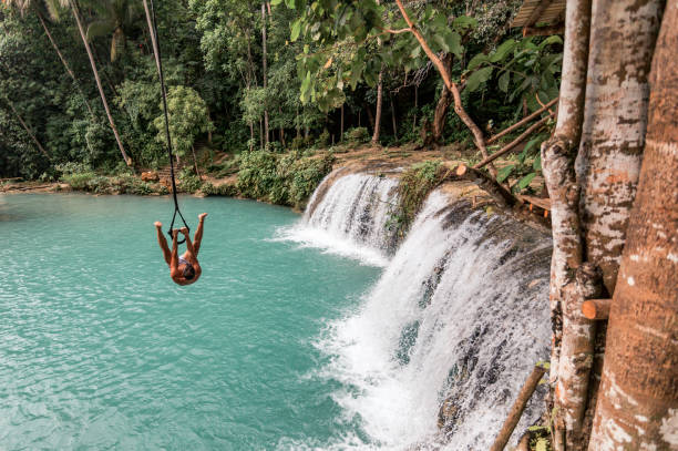 A young caucasian man plays with a rope swing over the Cambugahay Falls in Siquijor Island, Philippines A man playing with a rope swing in Cambugahay Falls siquijor stock pictures, royalty-free photos & images
