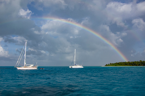 Sailing yacht anchoring unser a rainbow in the shallow waters of suwarrow atoll, cook islands, polynesia, pacific ocean