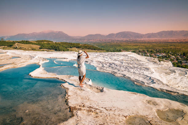 turkey, natural travertine pools and terraces in pamukkale. cotton castle in southwestern turkey, girl in white dress with hat natural pool pamukkale - mineral waterfall water flowing imagens e fotografias de stock