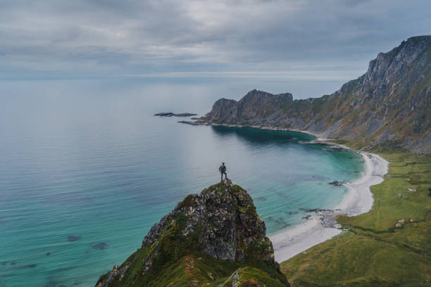 istock Man looking at Kvalvika beach while standing on rock 1214543526